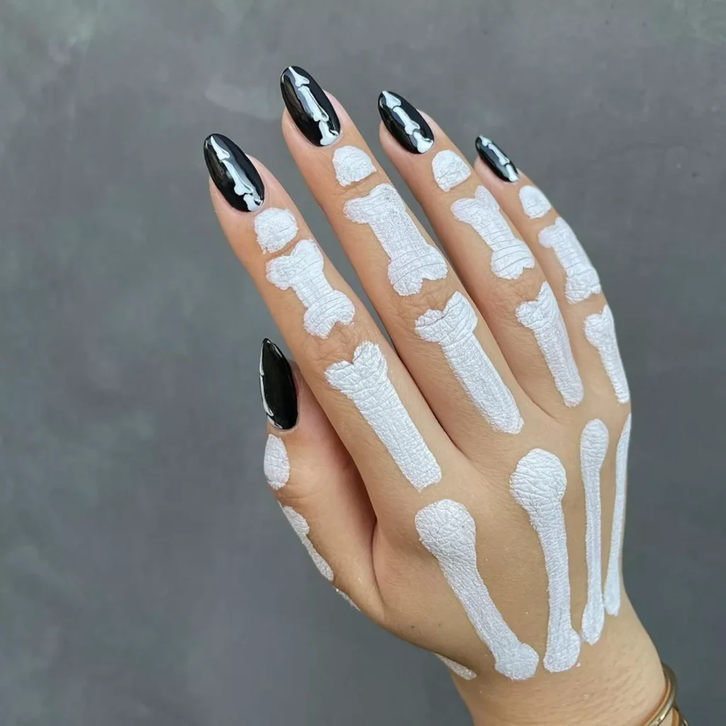 Glossy black halloween nails featuring white bone designs on sharp stiletto tips.