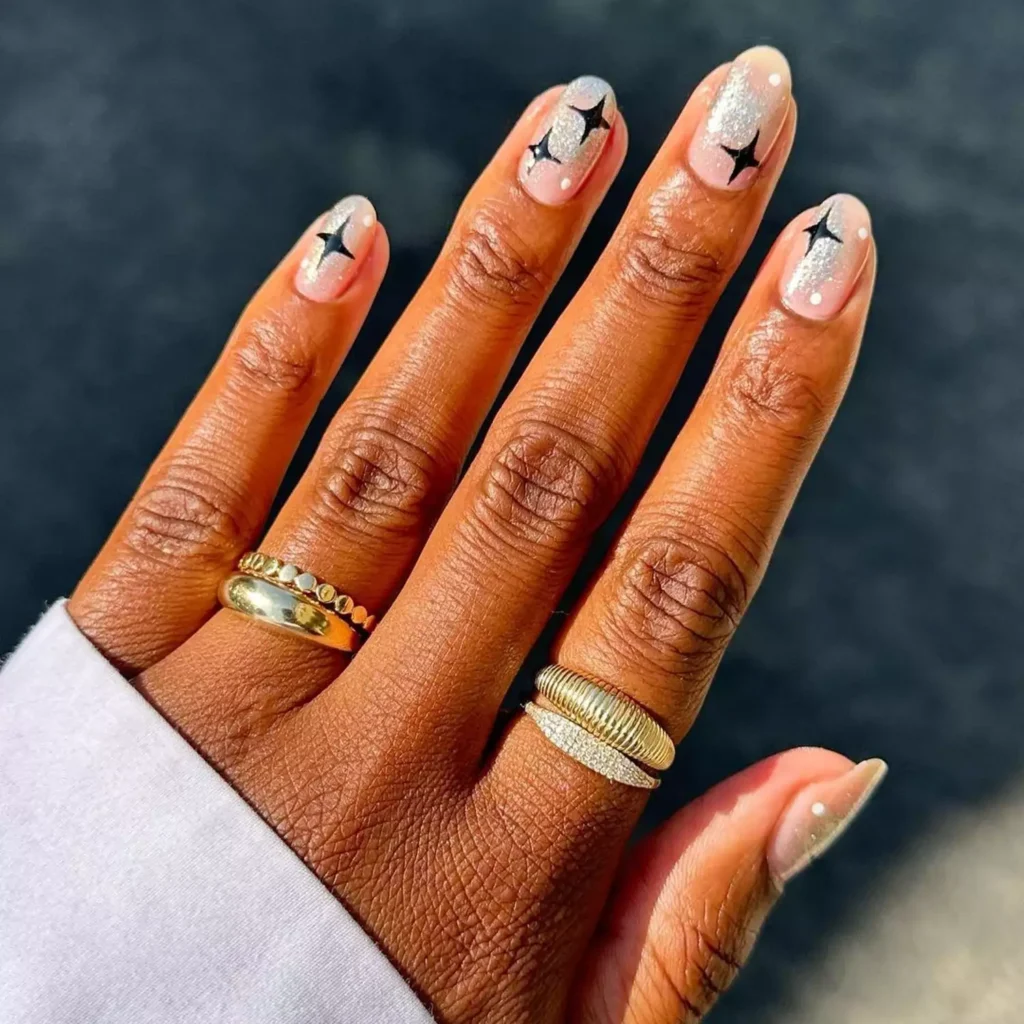 Elegant black halloween nails with silver glitter tips and delicate black star designs.