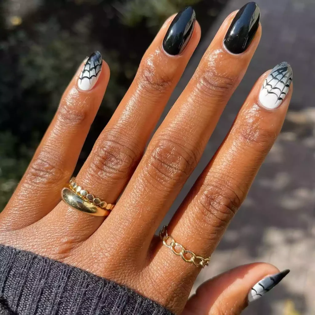 Glossy black halloween nails featuring white accent nails with delicate black spiderweb art.