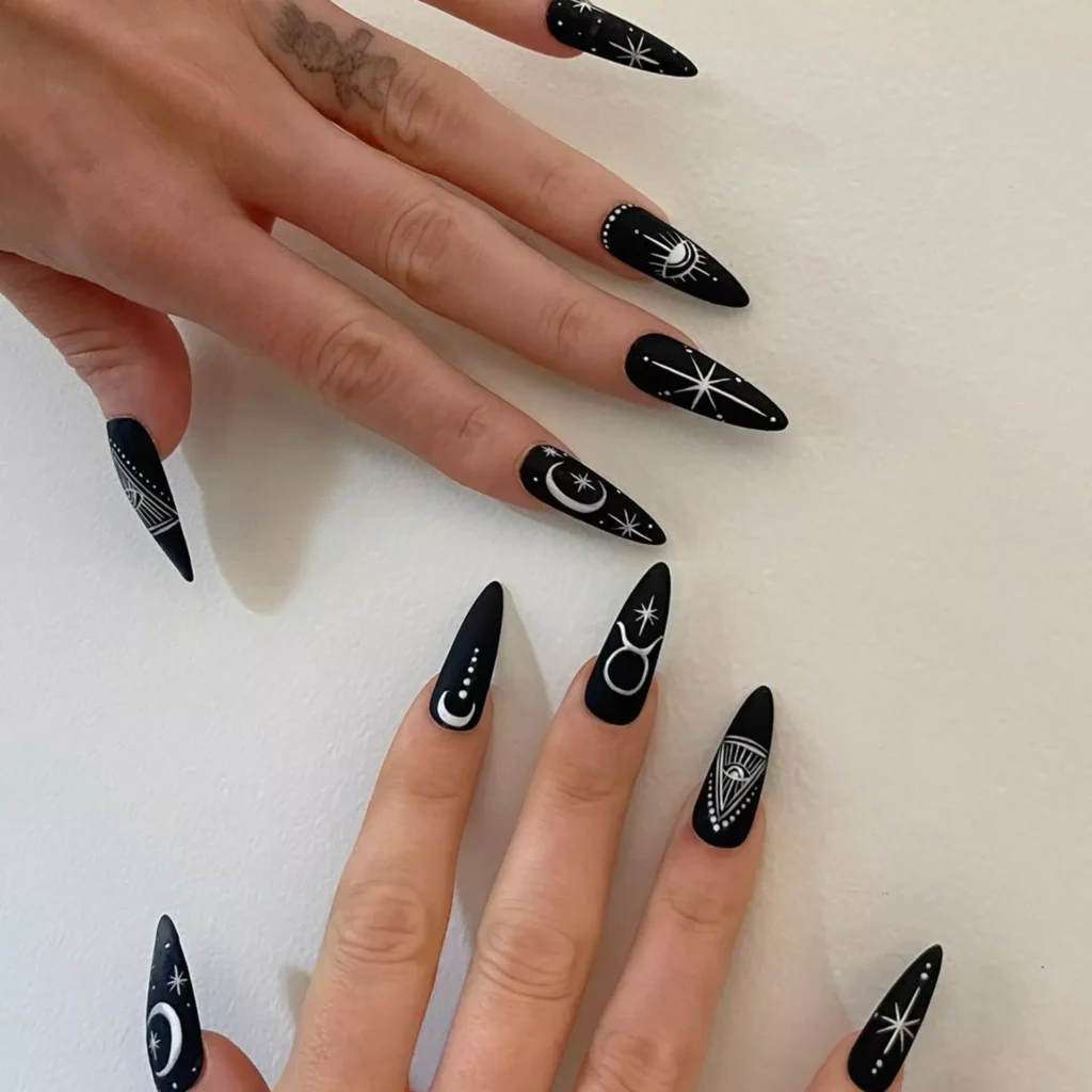 Matte black halloween nails with white stiletto tips showing moons, stars, and zodiac symbols.